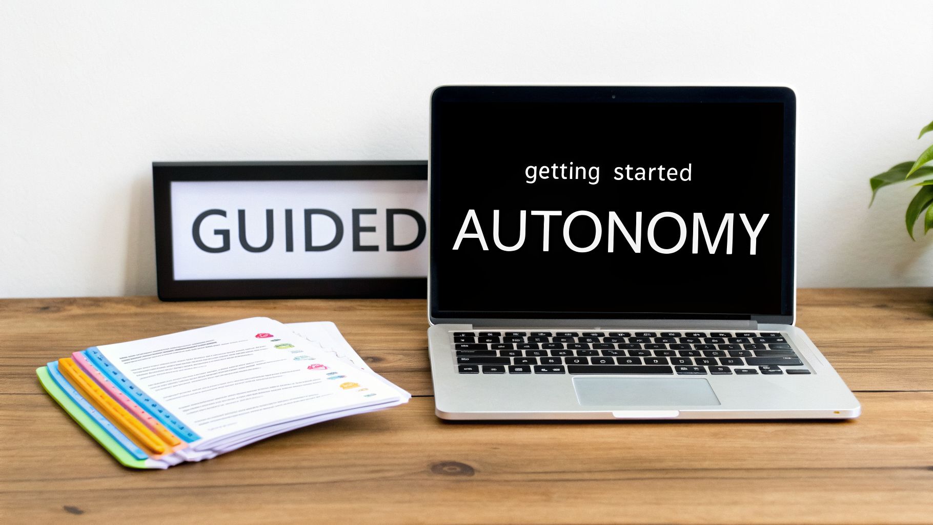 A laptop screen displays 'AUTONOMY' with 'getting started' above it, next to a 'GUIDED' sign and colorful documents.